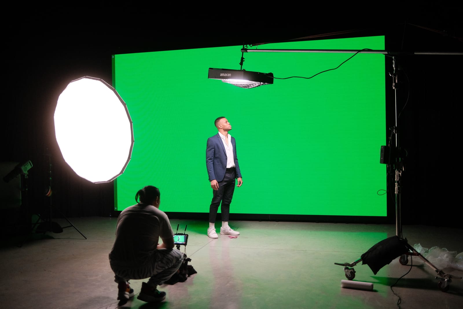 A crew member operating a camera while a subject stands against the LED wall lit green for keying